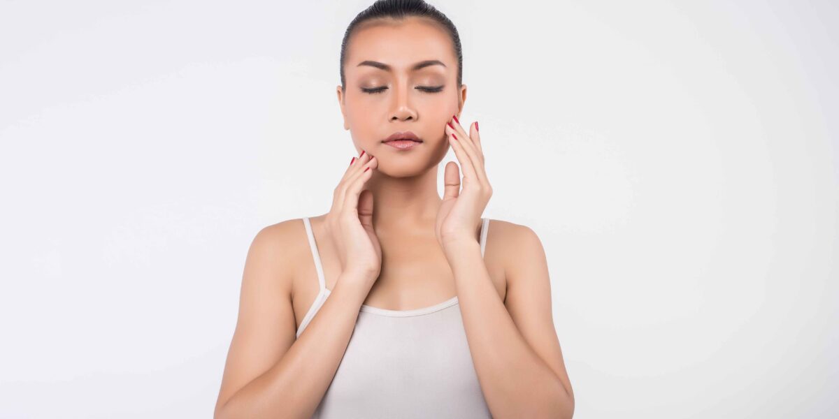 Beautiful young woman with clear fresh skin gently touching her face