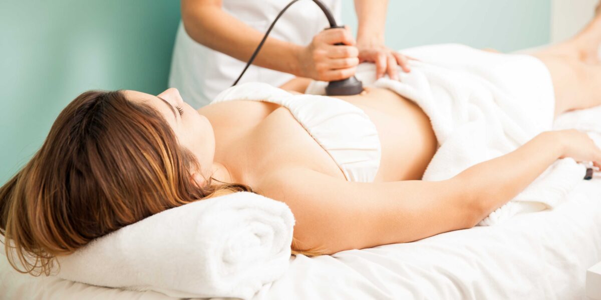 Female therapist performing body contouring treatment on client focusing on abdominal area